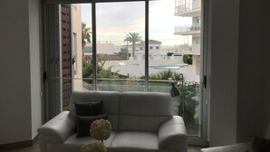Een moderne woonkamer met een grote schuifpui naar een balkon met uitzicht op een zwembad en gebouwen.