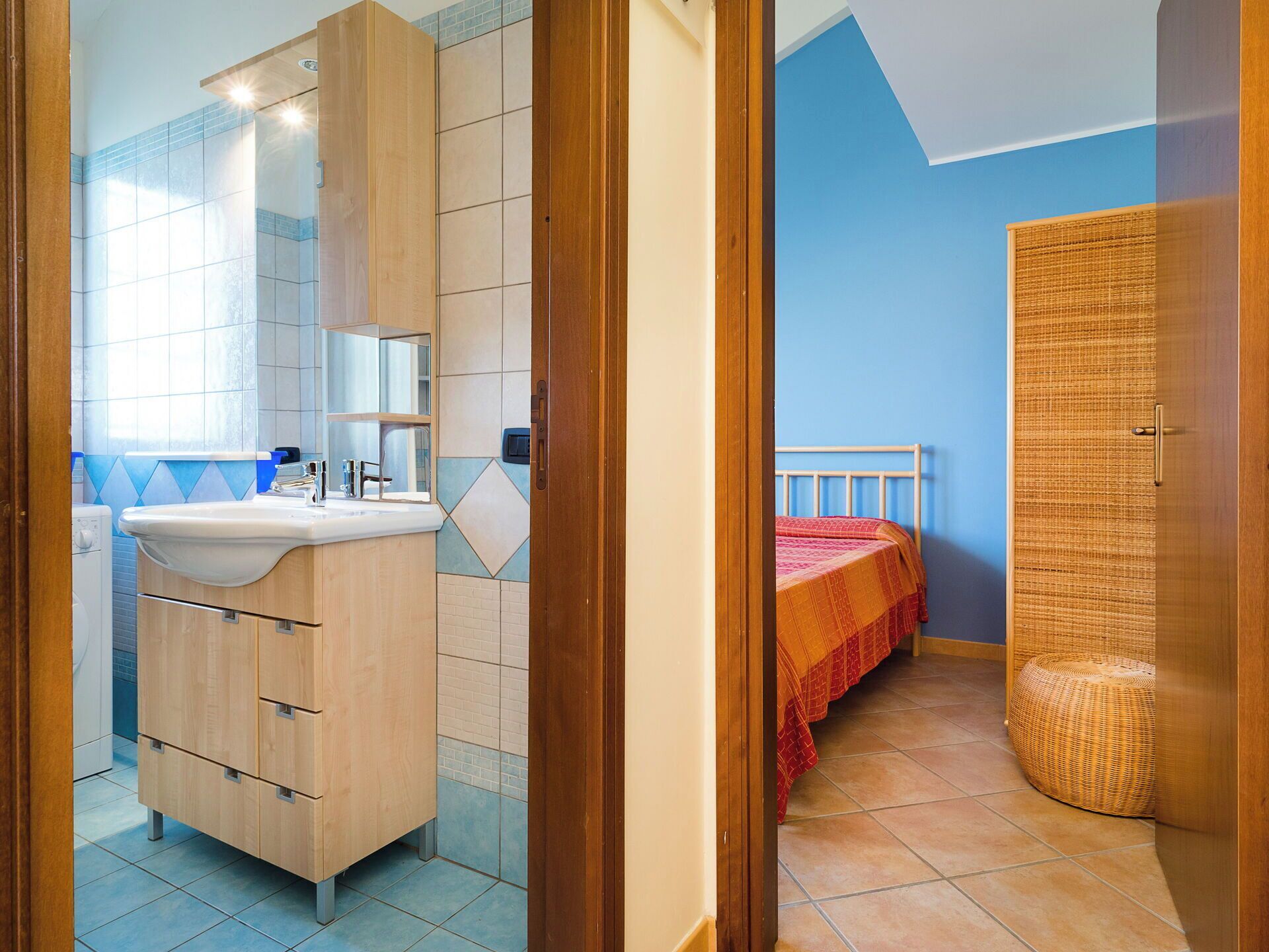 Une chambre à coucher avec un lit, une armoire en bois et une salle de bain équipée d’un lavabo et d’un miroir.