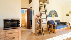 Un espace de vie compact comprenant un coin cuisine, un canapé, une échelle et une petite salle de bain.