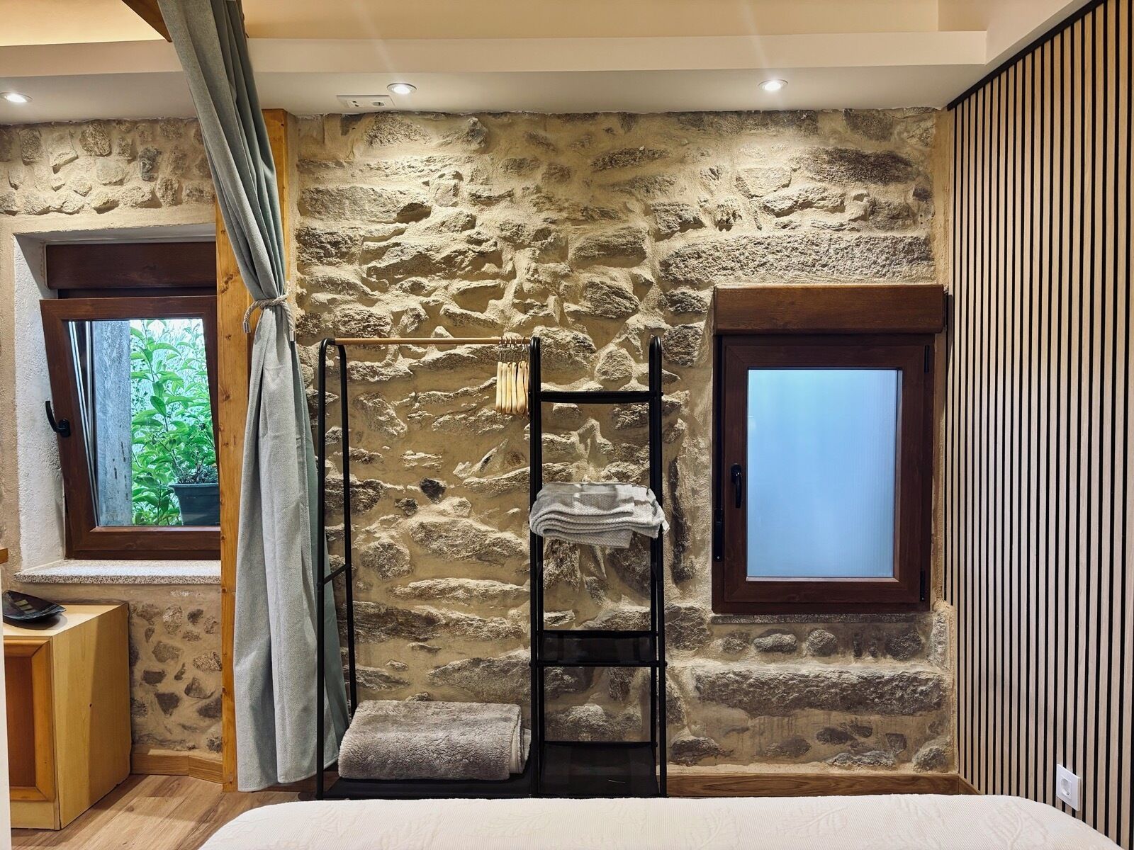 A bedroom with a stone wall, a wooden bench, a window, and a door.