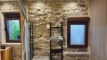 A bedroom with a stone wall, a wooden bench, a window, and a door.
