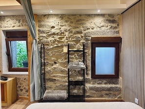 A bedroom with a stone wall, a wooden bench, a window, and a door.