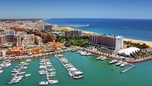 Un port de plaisance où sont amarrés de nombreux bateaux, un hôtel en bord de mer et, au loin, une vue sur la ville.