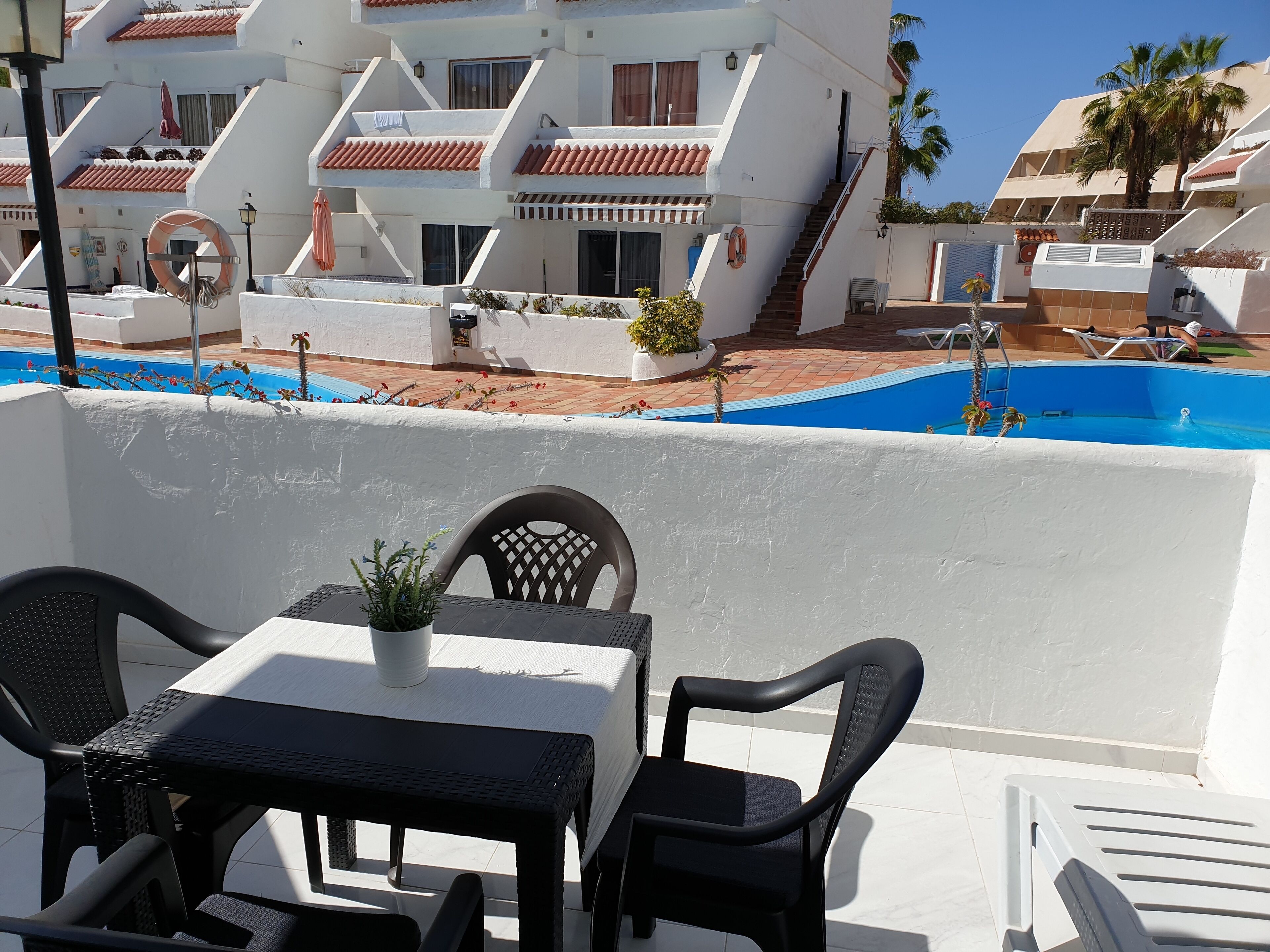A terrace with a table and chairs, a pool, and a white building with red-tiled roofs.