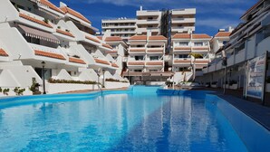 Une piscine à l’eau d’un bleu cristallin, entourée de bâtiments blancs aux toits recouverts de tuiles rouges et dotés de balcons.