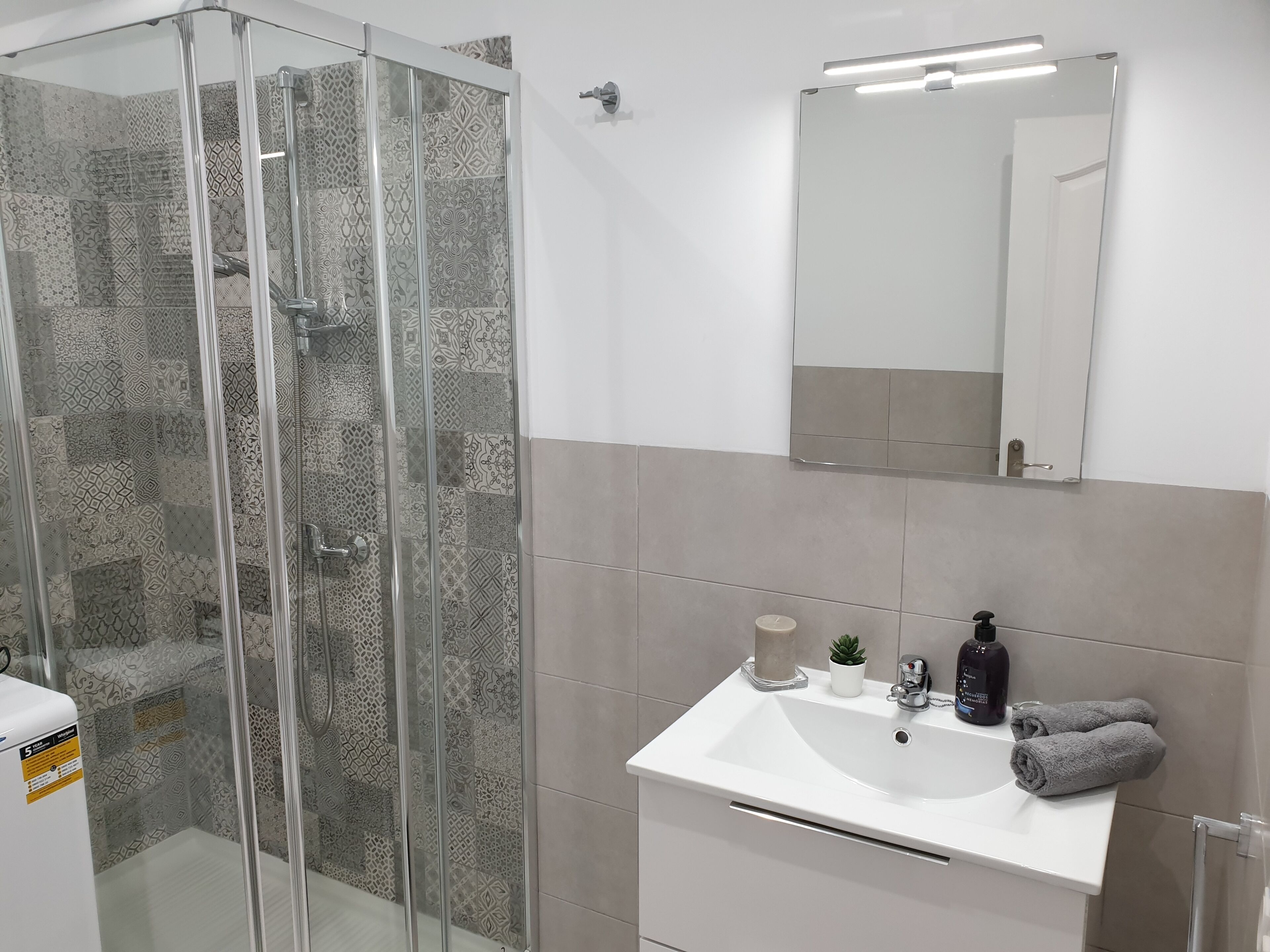Un baño con cabina de ducha de vidrio, lavamanos blanco, espejo y toalla.