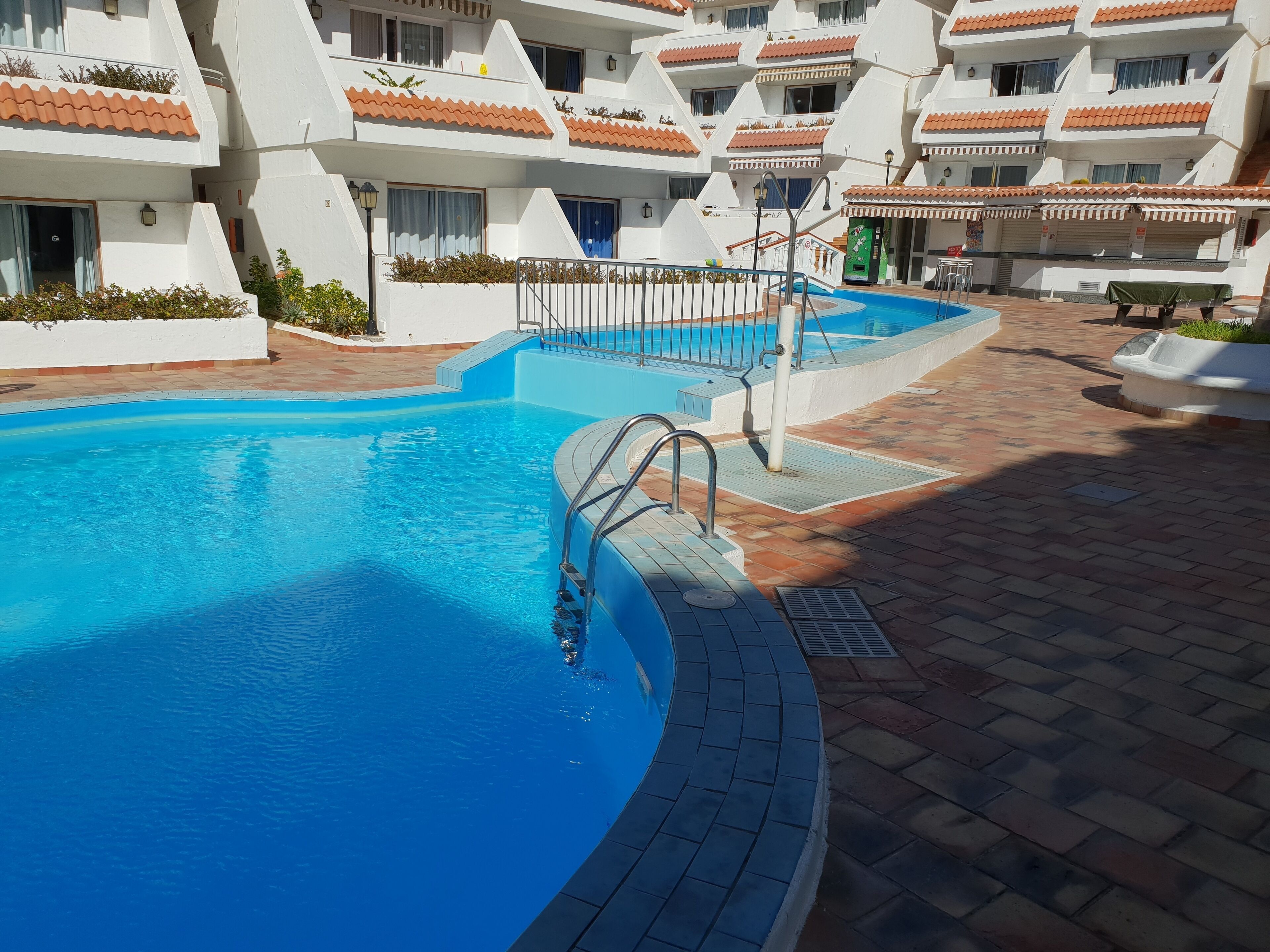 A swimming pool with a tiled deck, surrounded by multi-story buildings with balconies.