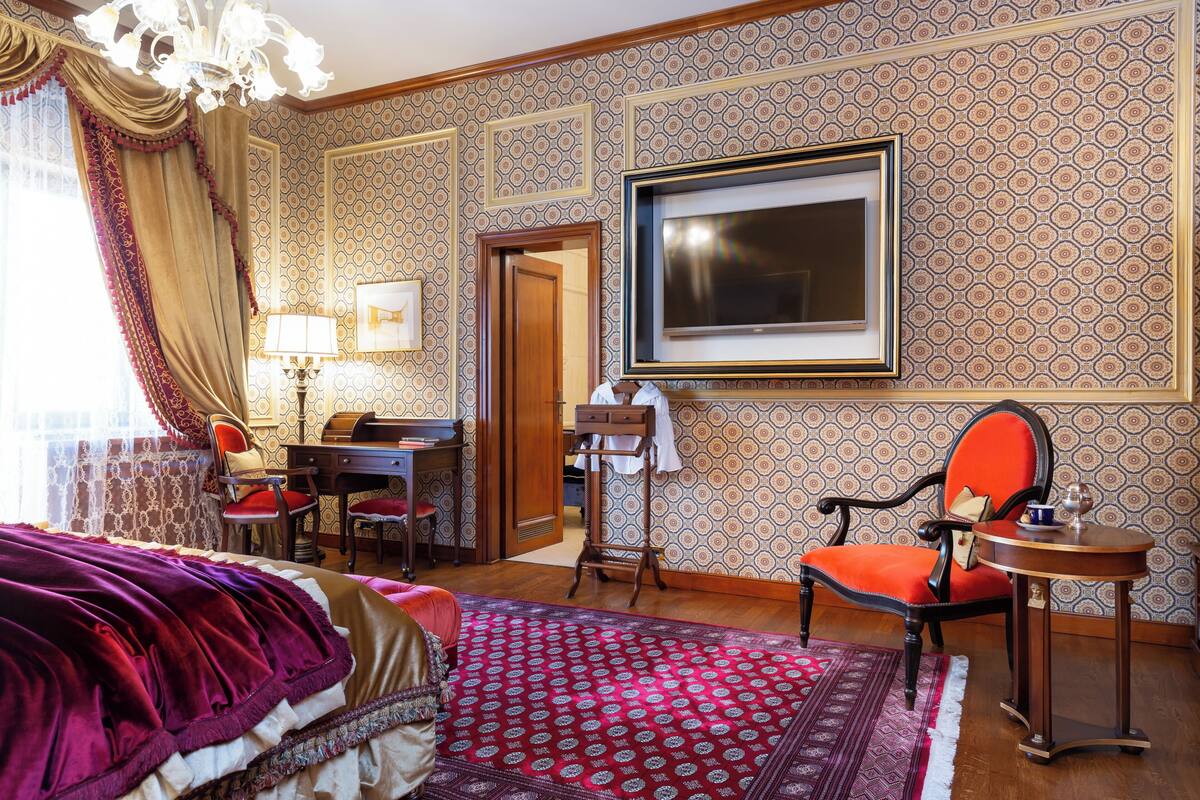 A hotel room with a bed, a desk, a chair, a television, and a patterned wall.