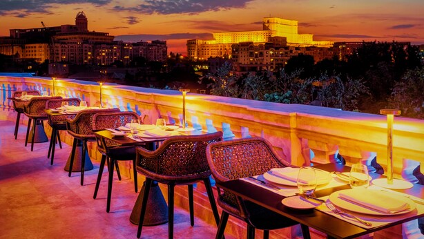 A rooftop dining area with tables set for two, overlooking a cityscape at sunset. - Suter Palace Heritage Boutique Hotel (Bucharest)