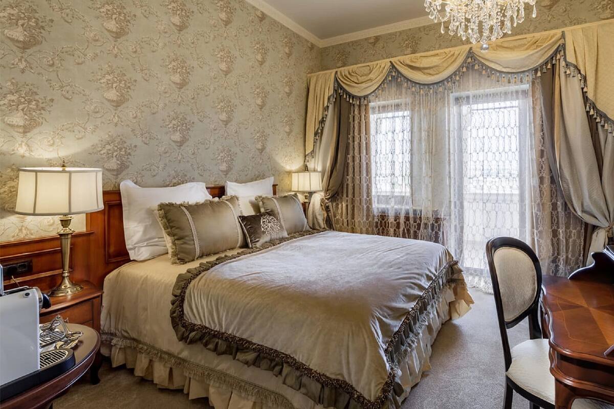 A classic bedroom with a large bed, two bedside tables, a desk, and a chair.
