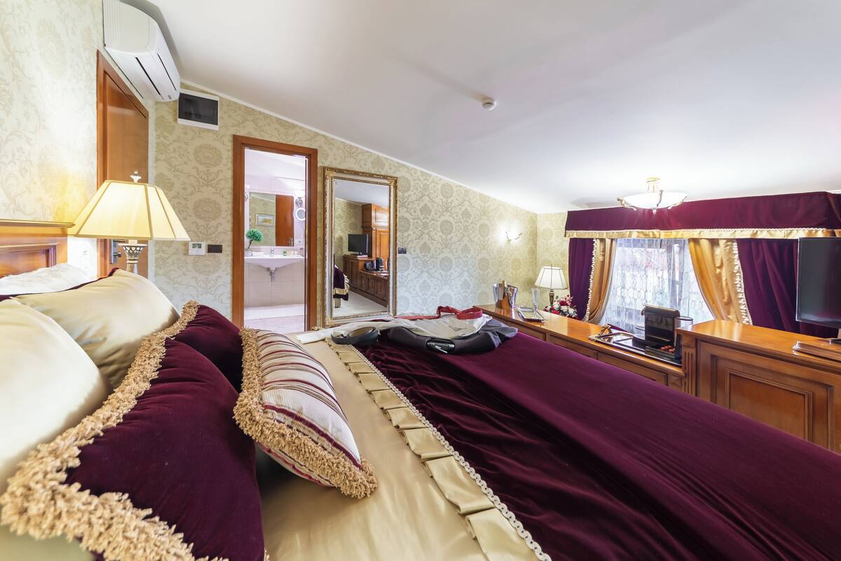 A hotel room with a large bed, a desk with a TV, and a bathroom visible through an open door.