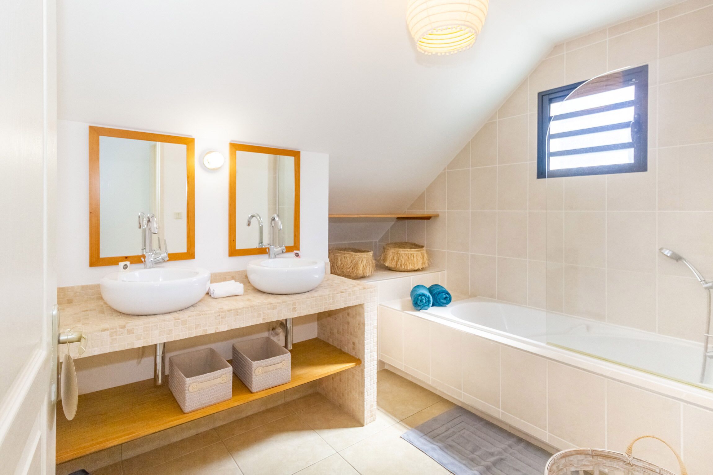 A modern bathroom with two sinks, a bathtub, and a window with blinds.