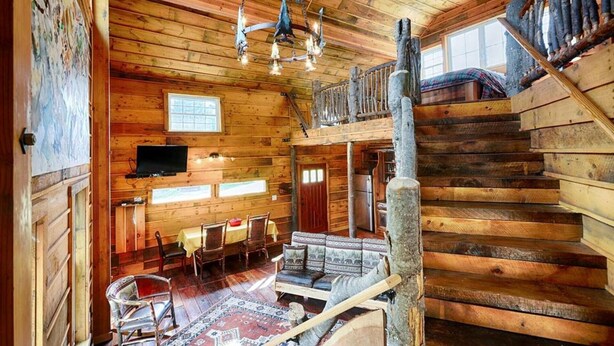 L’intérieur d’un chalet rustique comprend un coin repas, un escalier et un téléviseur.