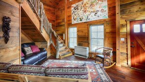 L’intérieur d’une cabane en rondins, avec un escalier en bois, un canapé, un fauteuil à bascule et un grand tableau abstrait.