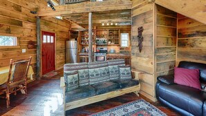 L’intérieur d’un chalet rustique est aménagé avec une table à manger en bois, un canapé, un divan en cuir noir et un coin cuisine équipé d’un réfrigérateur et d’une cuisinière.