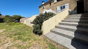 A building with a staircase leading to a door, a small bush, and a clear sky. - Quiet apartment and grounds. Sea view and maquis (Cargèse)