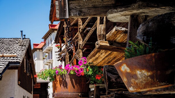 Eine enge Straße mit Holzbauten, einem hängenden Blumentopf und einer rustikalen Holzkonstruktion.
