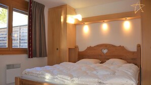 Ein Bett mit hölzernem Gestell und Herzform, weiße Bettwäsche und ein Fenster mit Vorhängen.