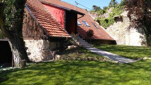 A rustic building with a sloped red-tiled roof, stone walls, and a small staircase leading to a red door. - Pretty cottage F2 of 50m ² independent in Rouffach (Rouffach)