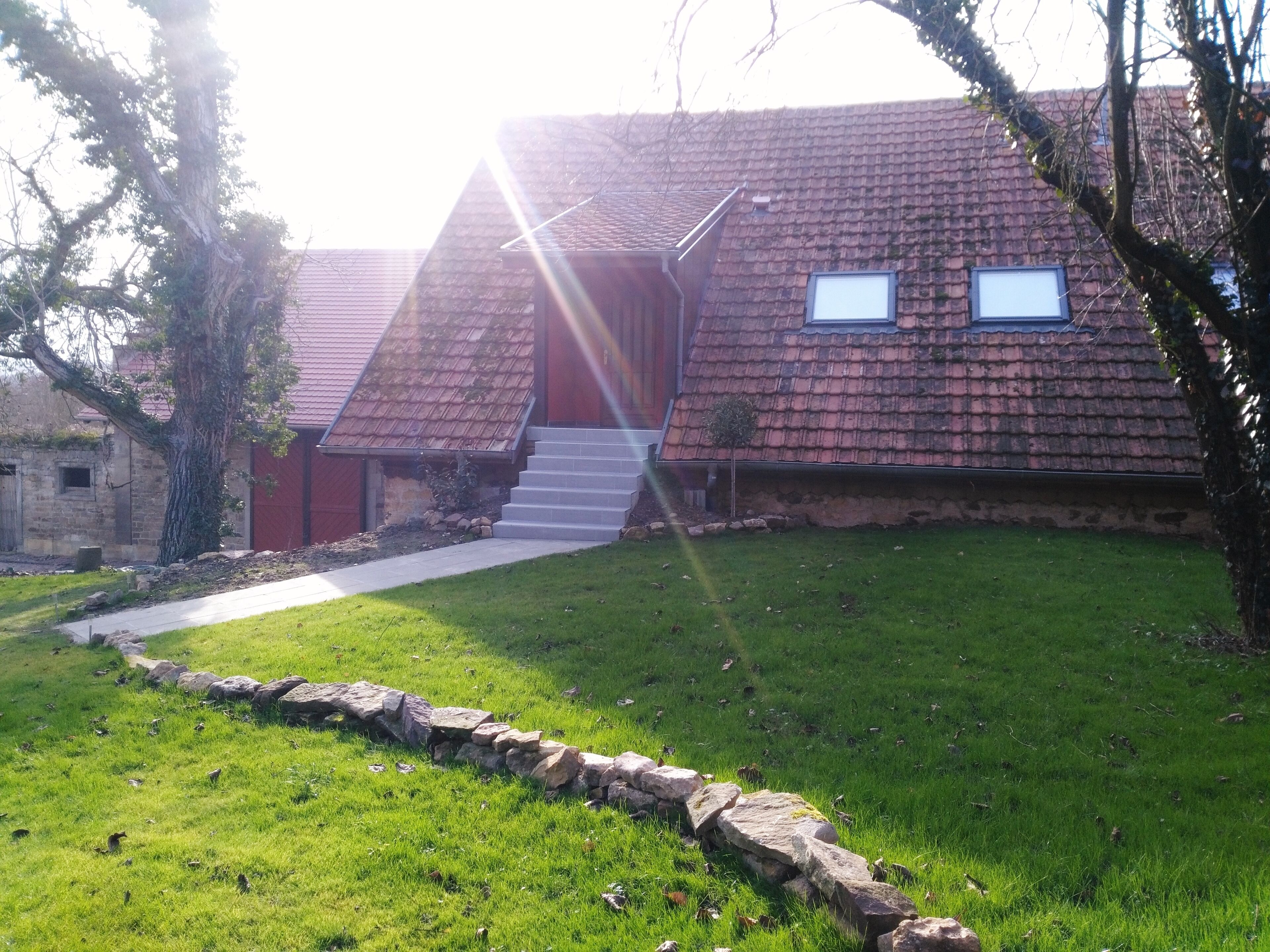 A house with a red roof, a stone pathway leading to the entrance, and a small tree in the front yard.