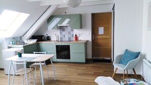 A modern kitchen with green cabinets, a dining area with a table and chairs, a white rug, and a blue chair with a cushion. - Pretty cottage F2 of 50m ² independent in Rouffach (Rouffach)
