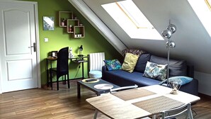 A loft-style room with a sloped ceiling, a sofa with patterned cushions, a small table with a lamp, and a chair. - Pretty cottage F2 of 50m ² independent in Rouffach (Rouffach)