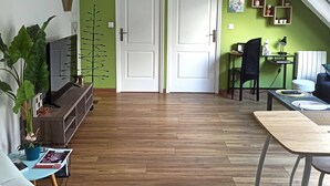 A spacious living room with a wooden floor, a sofa, a coffee table, and a dining table. There are two doors, a staircase, and a ceiling light fixture. - Pretty cottage F2 of 50m ² independent in Rouffach (Rouffach)