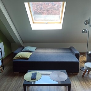 A modern loft bedroom with a skylight, a sofa bed, a small table with remotes, and a floor lamp. - Pretty cottage F2 of 50m ² independent in Rouffach (Rouffach)