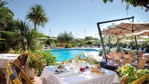 Un área de comedor junto a la piscina con mesas, sillas y sombrillas.