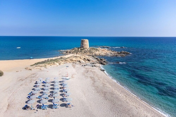 A beach with a tower, clear blue water, and sun loungers.