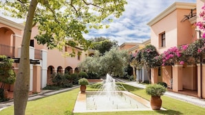 Un patio con una fuente, rodeado de edificios con ventanas arqueadas y balcones.