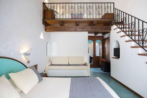 A bedroom with a bed, a sofa, a staircase, and a hallway leading to a bathroom.
