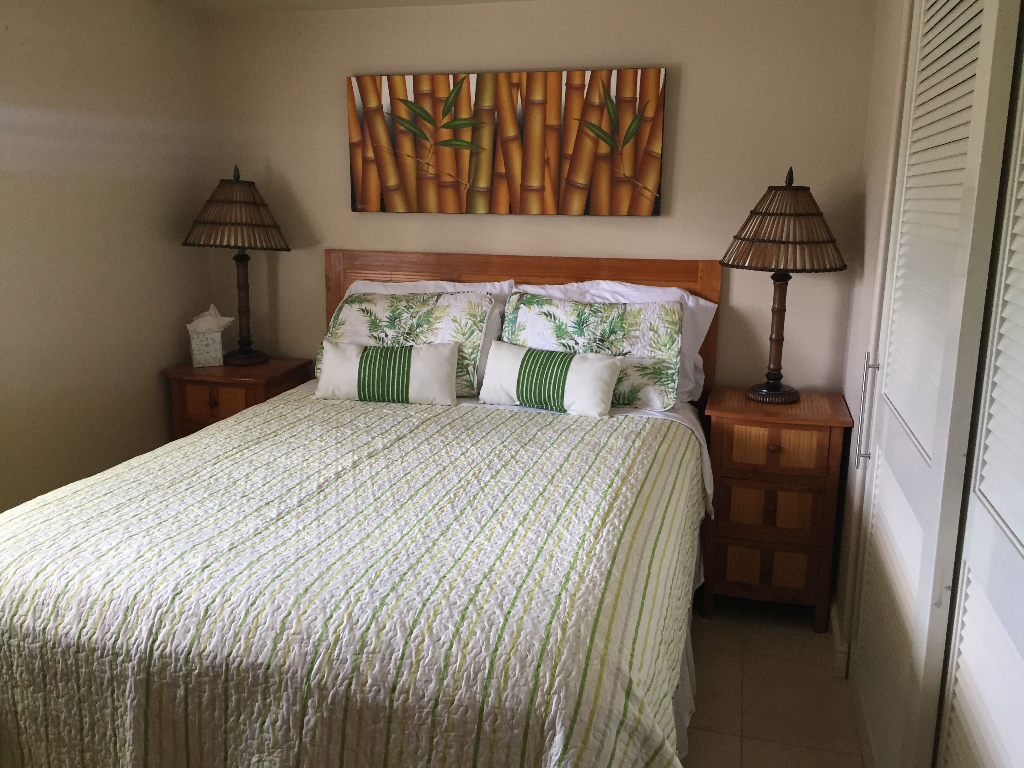 Un lit bien fait, recouvert d’une couvre-lit à rayures, avec deux lampes de chevet et une décoration murale sur le thème du bambou.