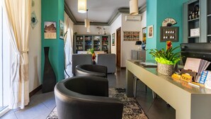 A hotel lobby with a reception desk, seating area, and a bookshelf. - Albergo Residenziale La Corte (Tortoli)