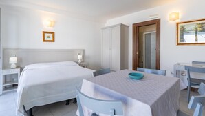 A hotel room with a bed, a table with chairs, a small table with a bowl, a wardrobe, and a painting on the wall. - Albergo Residenziale La Corte (Tortoli)