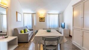 A dining area with a table, chairs, a sofa, a television, and a cabinet. - Albergo Residenziale La Corte (Tortoli)