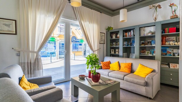 A living room with a sofa, armchairs, a coffee table, and a bookshelf. - Albergo Residenziale La Corte (Tortoli)