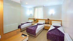 Habitació d'hotel amb tres llits individuals, un escriptori de fusta, un mirall i una finestra amb cortines.