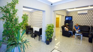 Rebedor amb taulell de recepció, zona de seients, plantes en testos i un televisor.