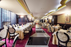Uma sala de conferências de hotel com várias mesas e cadeiras, um tapete vermelho e uma janela grande com persianas.