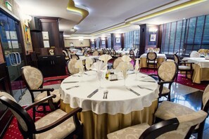 Un comedor formal con mesas redondas, sillas y una alfombra roja.