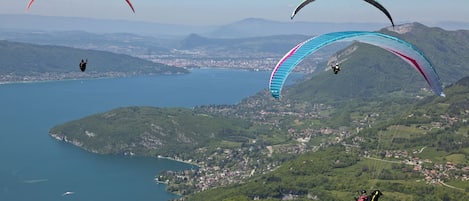 Una vista panorámica de un lago rodeado de colinas, con varios parapentistas volando.