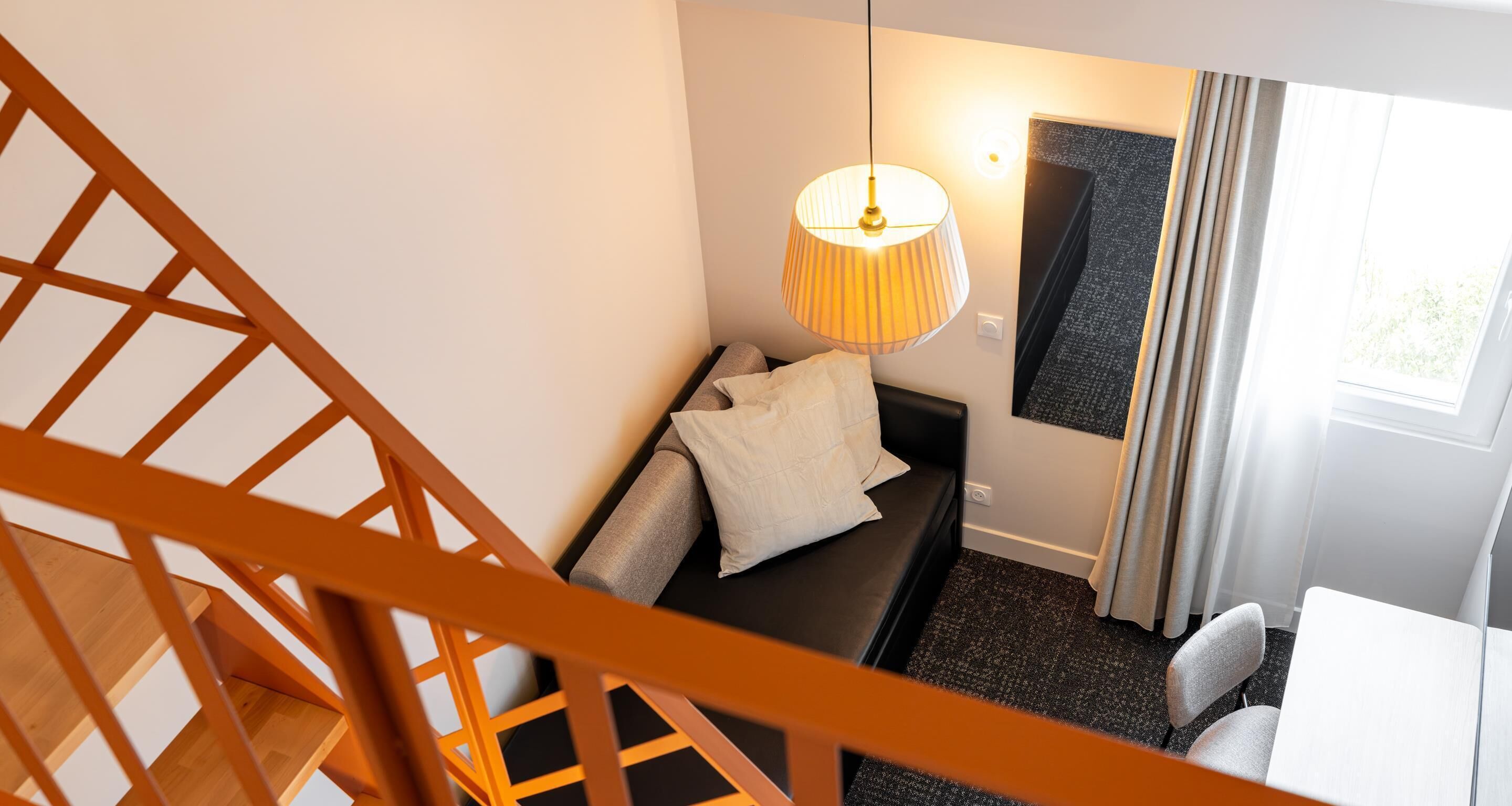 A modern room with a staircase, a sofa, a lamp, and a window with curtains.