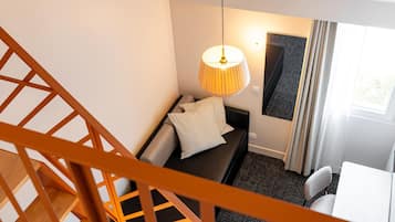 Quarto moderno com escada, sofá, luminária e janela com cortinas.