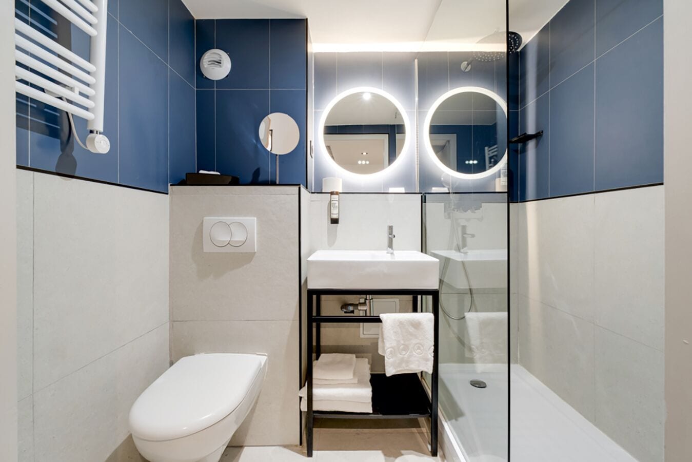 A modern bathroom with a white toilet, a glass-enclosed shower, and a white sink with a mirror above it.