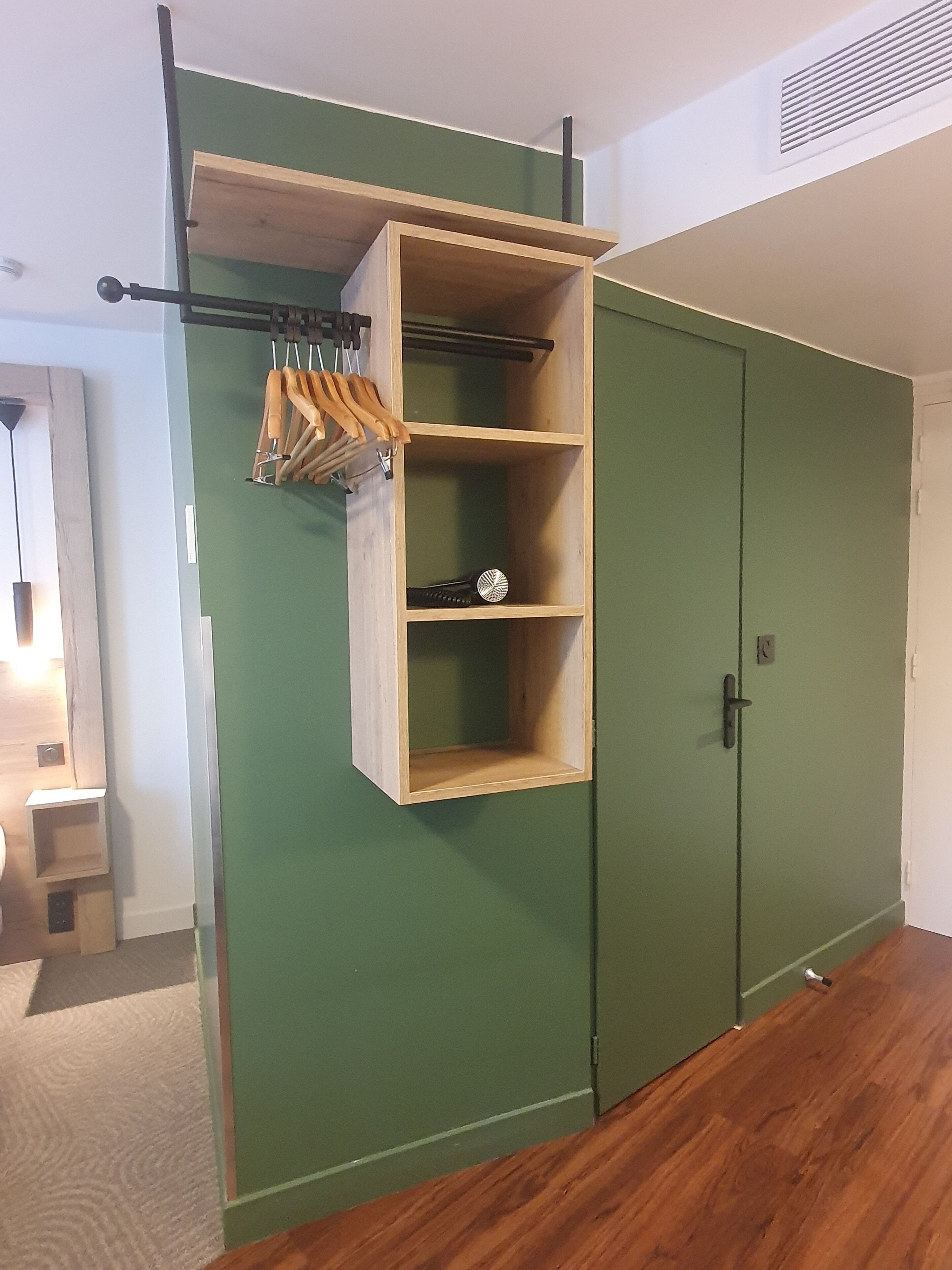 Una habitación con pared verde, un estante de madera con utensilios de cocina colgantes y un armario cerrado.