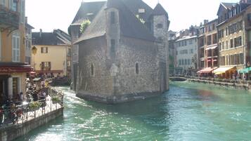 A historic stone building with a tower, situated by a canal with cafes and boats.