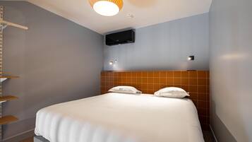 A hotel room with a bed, a mounted TV, and a shelf unit.