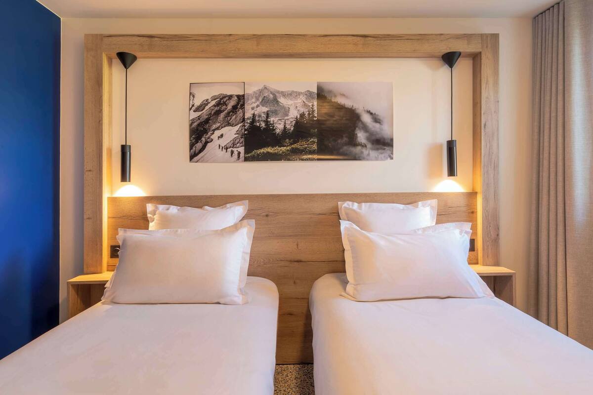 A hotel room with two beds, wooden headboard, and wall-mounted artwork.