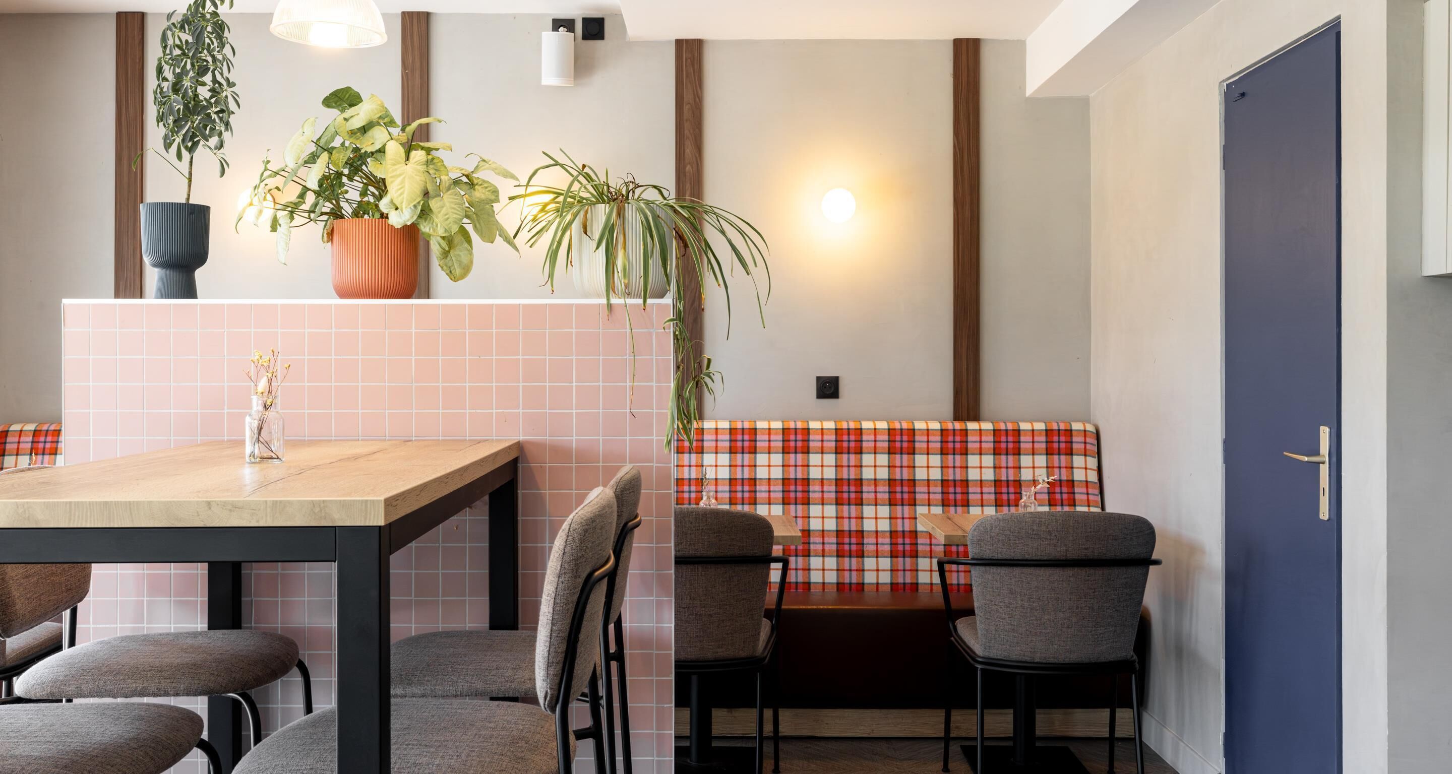 Une cuisine moderne avec une table en bois, des chaises grises, un banc à carreaux rouges et blancs, et des plantes en pot.